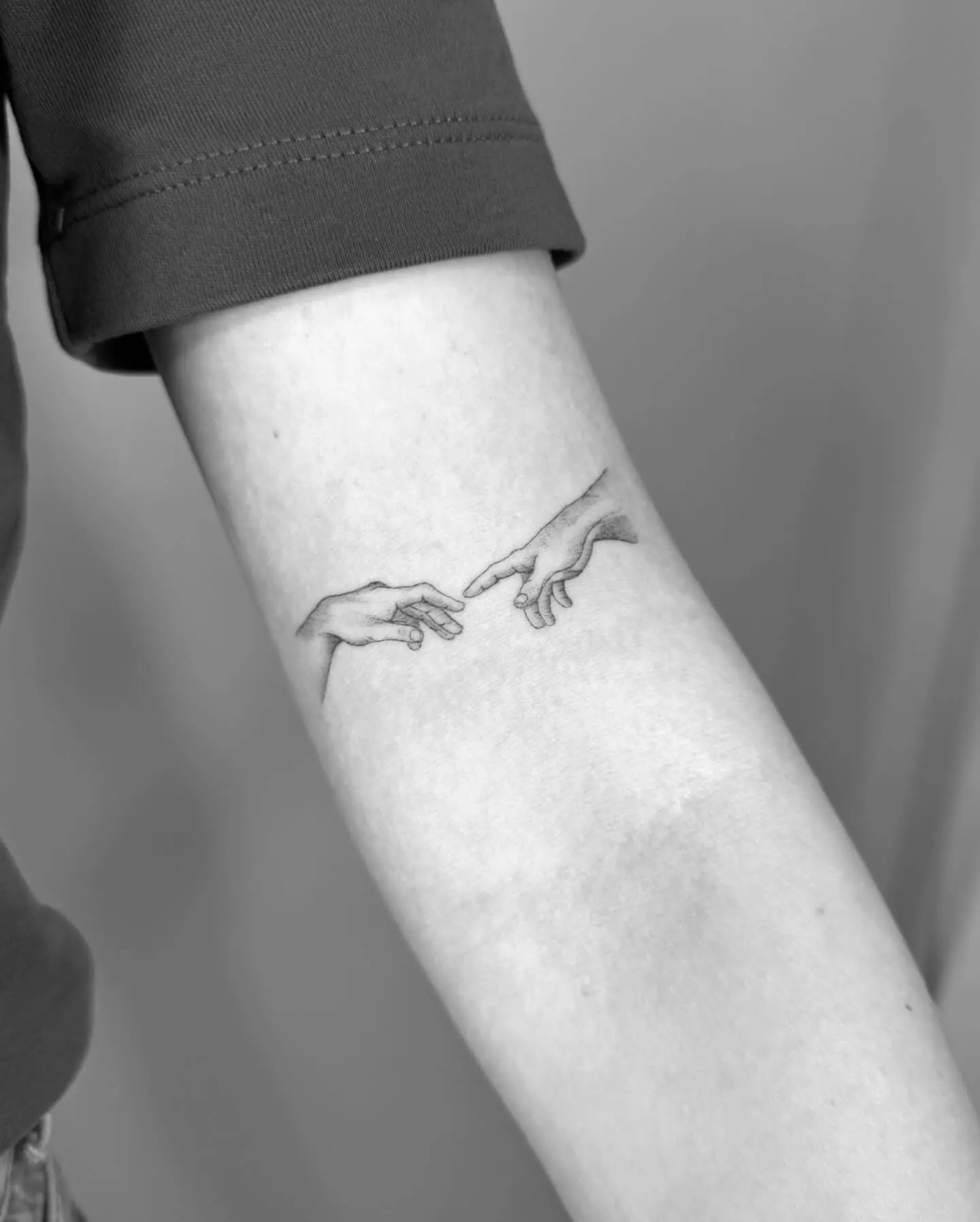 Fine Line Tattoo zweier sich berührender Hände nach Michelangelo am Unterarm