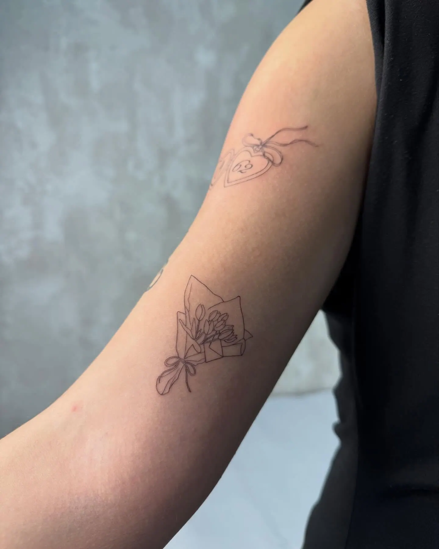 Fine Line Tattoo mit Herzanhänger und Zahl sowie einem Tulpenstrauss am Arm